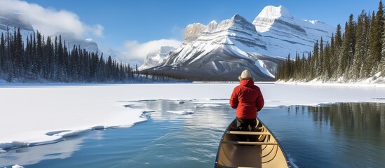 a man in winter coat riding in canoe on turquoise lake in Spirit Island on Maligne Lake Canada with view of mountains - obrazy, fototapety, plakaty