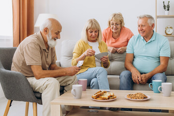 Group of senior people laughing while relaxing at home and playing cards.