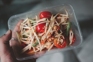 Man holding a box of Thai papaya salad spicy flavor, it tastes sour, sweet and spicy.