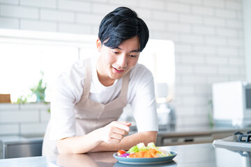 料理を見ながら考えるエプロンをつけた若い日本人男性