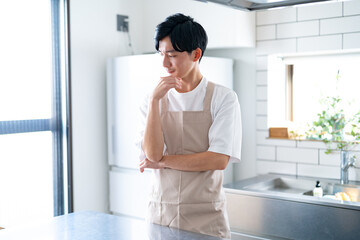 キッチンで考えるエプロンをつけた若い日本人男性
