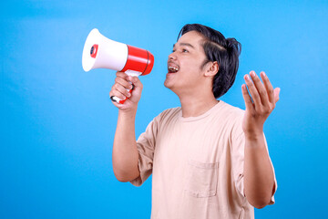 Young smiling Asian man wear basic t-shirt scream in megaphone announces discounts sale or good news
