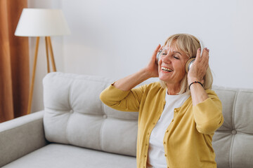 Happy senior woman wearing headphones while listening to music at home