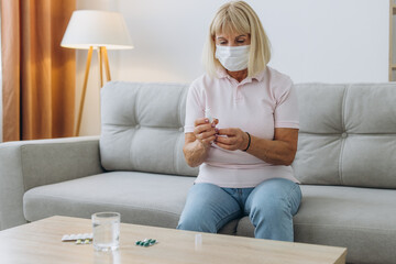 Senior woman in face medical mask using hand antibacterial liquid sanitizer at home