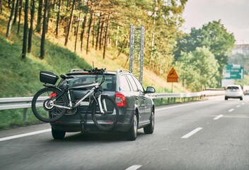 On the Road with Bikes. Car-mounted Trunk Bicycle Transport. Back view car with mounted bike tail carrier driving on highway road