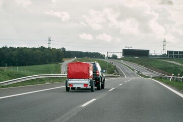SUV with trailer goes on the highway. Moving stuff with a small rentable trailer. - obrazy, fototapety, plakaty