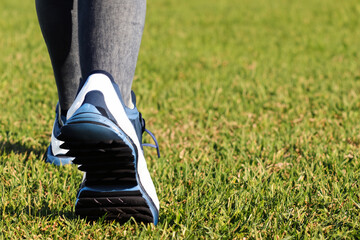 the girl walks on the grass. female nails in leggings and blue sneakers walk along green grass, close-up view - obrazy, fototapety, plakaty