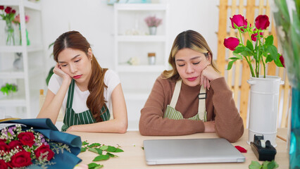 Two young Asian woman florist bored working at flower shop don't have order from customer. Woman...