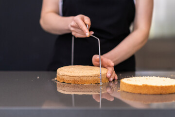 Skilled woman using string knife for separating cake layers in modern kitchen female confectioner...