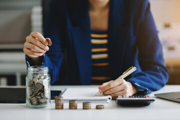 businesswoman holding coins putting in glass with using smartphone and calculator to calculate...