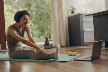 Young woman in sportswear and headphones at home does a warm up and stretch exercises on mat