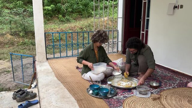 A couple prepare to make sour dough wheat flour and fermentation to bake flat Turkish bread Iran country life country side rural town village people local skill bakery outside in clay wood fire oven