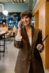 Excited business woman talking on mobile phone while standing in office lobby