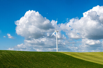 Eolienne au milieu de champs verts sous un ciel bleu avec des nauges