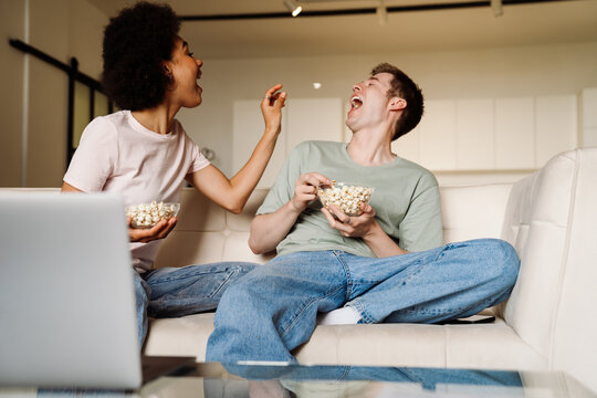 Happy couple having fun and throwing popcorn while watching movie at home