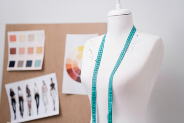 Tape measure and pins on dummy near corkboard with swatches and sketches in dressmaking shop...