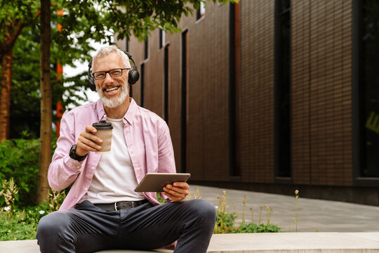 Senior man using tablet and drinking coffee while sitting outdoors