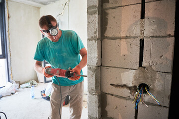 Male construction worker drilling brick wall with electric drill in apartment under renovation. Man...