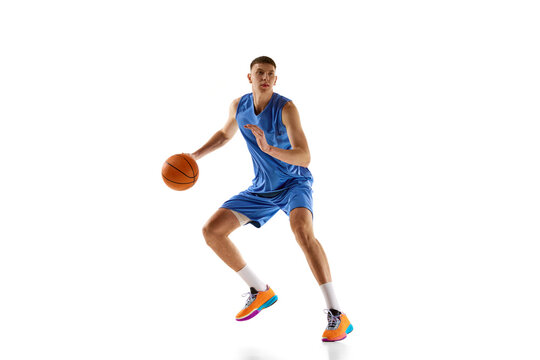 Dynamic image of young man in blue uniform, basketball player in motion during game, dribbling ball isolated on white background. Concept of sport, competition, match, championship, health, action. Ad