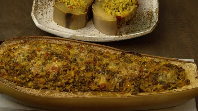 Baked squash stuffed with basmati rice, tomatoes, mung beans, and cheese.Two slices on a plate and a whole piece of pumpkin cut lengthwise on baking paper. Table spin.   