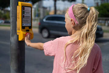 Little girl pushing the crosswalk button.importance of kids learning traffic safety on traffic...