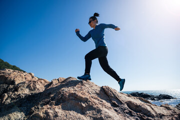 Woman runner running on sunrise seaside rocky mountains