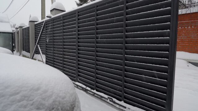View of automatic gate closing at snowy winter day. Modern design motorized automatic driveway gate, fence gate of courtyard of residential building in winter.