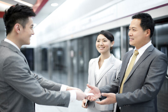Businessman handing over business card to new friends on subway platform - Powered by Adobe