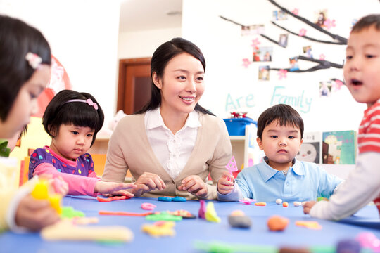 Kindergarten teacher and children playing with plasticine