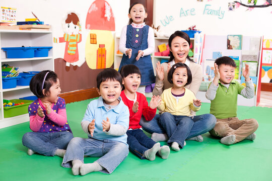 Female teacher and cute kindergarten children clapping hands and singing