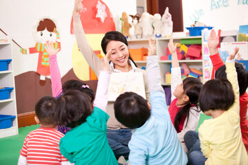 Cute kindergarten children raising hands to answer female teacher's question