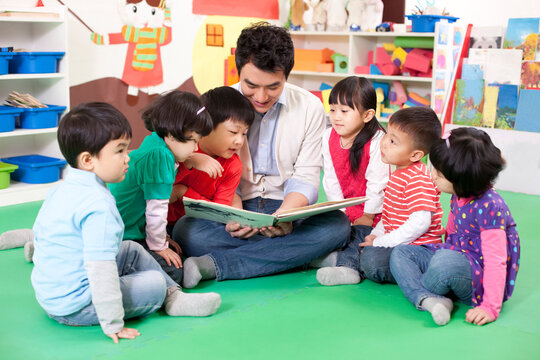 Male teacher reading picture book with cute kindergarten children