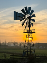 Bright orange sunrise at fields with light fog and an American style windmill