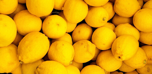 A top view of many bright yellow lemons. The lemons cover the entire background of the image, creating a vibrant and refreshing scene, the natural beauty and color of the citrus fruits.