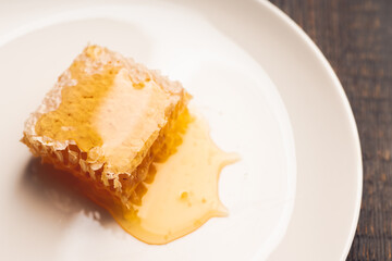 Fresh honeycomb with liquid honey on the white plate. Selective focus.