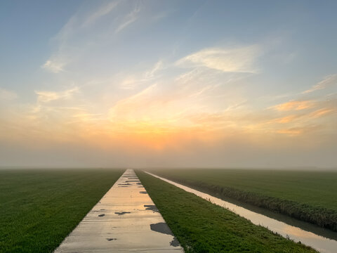 Wet country dirt road at sunrise with canal or sloot between meadow in Friesland