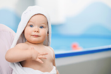 Portrait happy baby girl in white towel in arms of his mother after swimming lessons in pool