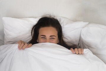 In the soft cocoon of her bed, a contented woman wears a morning smile, hiding beneath a white...