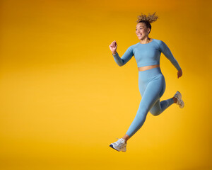 Fototapeta premium Studio Shot Of Woman Wearing Gym Fitness Clothing In Mid-Air Exercising On Yellow Background