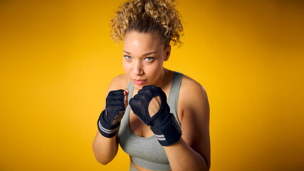 Studio Shot Of Woman Wearing Gym Fitness Clothing In Boxercise Class Sparring On Yellow Background