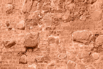 Background from a wall of old red bricks and stones, peach fuzz tinting.