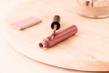 Liquid lipstick, blush and makeup powder on a wooden board, peach fuzz tinting.