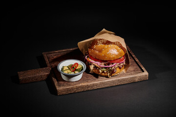 delicious hamburger with sesame bun, beef and pickles as side dish on wooden tray on black