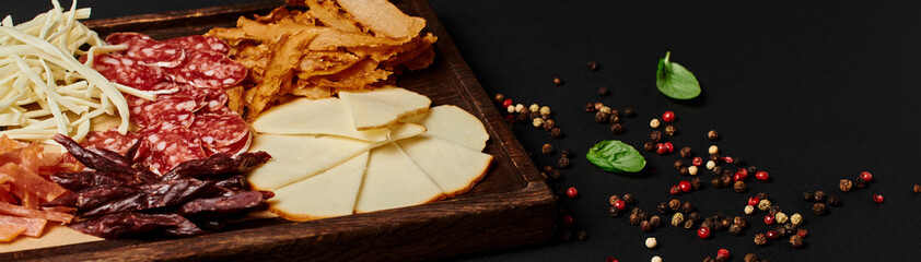 charcuterie board with gourmet cheese selection, dried beef and salami slices on black, banner