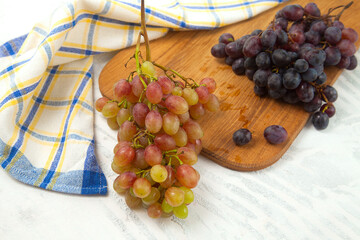 Cutting board with bunches of organic pink and dark blue grapes on white wooden background..