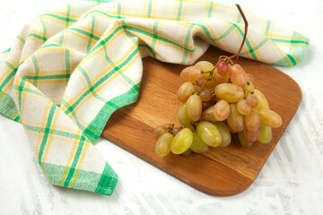 Cutting board with bunch of organic pink grapes on white wooden background..
