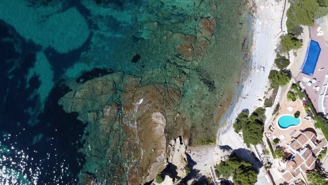 Top-down shot of transparent blue water rock beach.