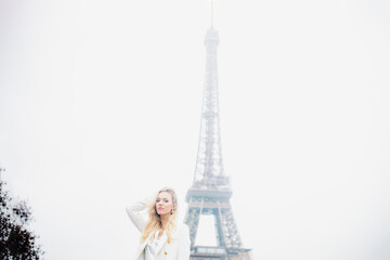 Pretty blonde girl with long hair poses against background of sky and Eiffel Tower.Tourism. 