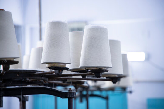 White Cotton Spools of Thread on the industrial knitting factory machine stand - Powered by Adobe