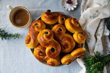 Plate with pile of homemade Swedish saffron buns lussekatter and cup of espresso coffee on linen tablecloth .